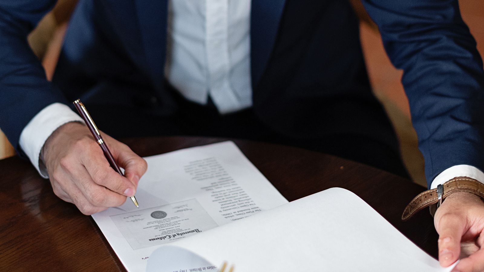 Professional in a suit signing official paperwork at a desk