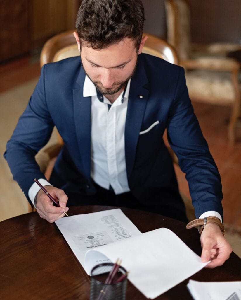 A consultant in a navy suit signing attestation paperwork at an office desk