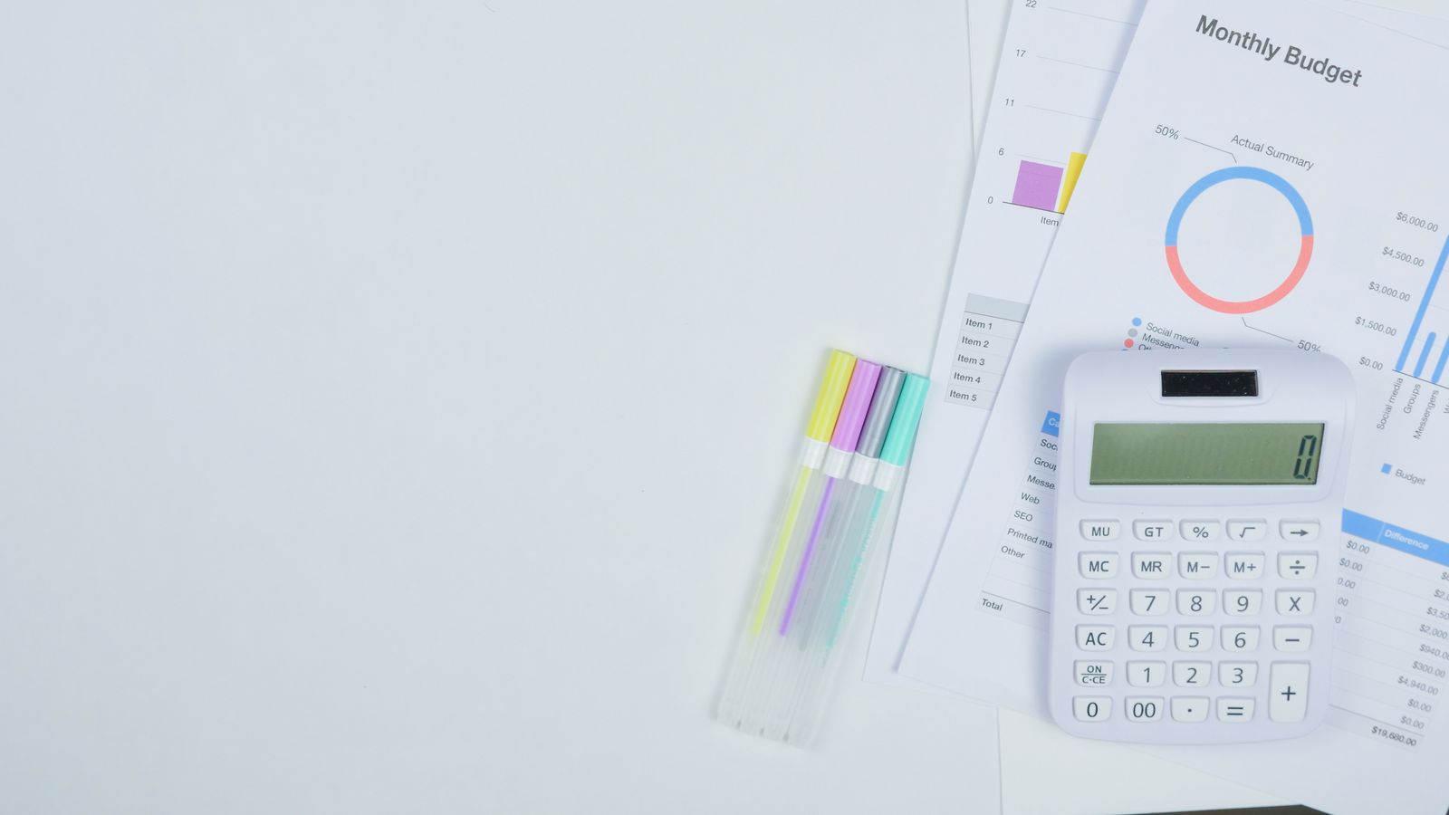 White calculator beside printed budget charts on a clean desk