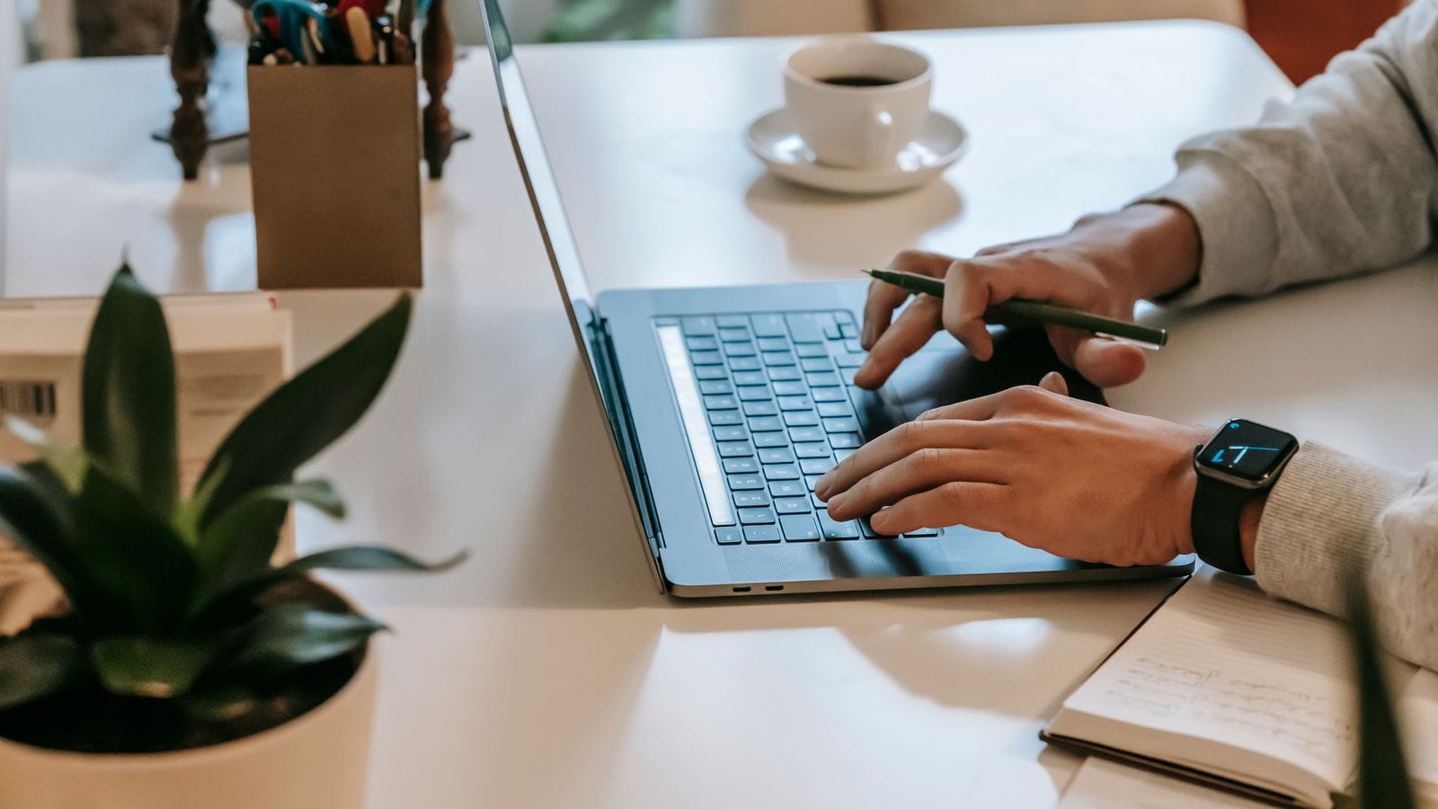 Hands typing on a laptop at a desk, checking status online